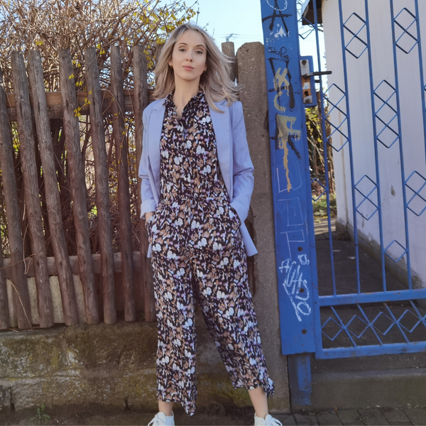 Frau in Jumpsuit und Blazer vor einem Zaun und blauer Tor.