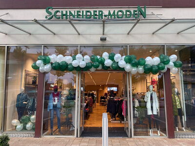 Außenansicht eines Modegeschäfts mit grünen und weißen Ballons und dem Schriftzug Schneider-Moden.