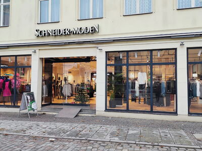 Außenansicht eines Modegeschäfts mit dem Schriftzug „Schneider-Moden“ und Schaufenstern.