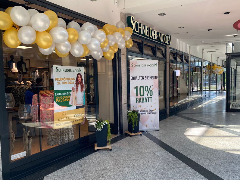 Schaufenster des Ladens Schneider-Moden mit goldenen und weißen Ballons und Rabattaktionen.